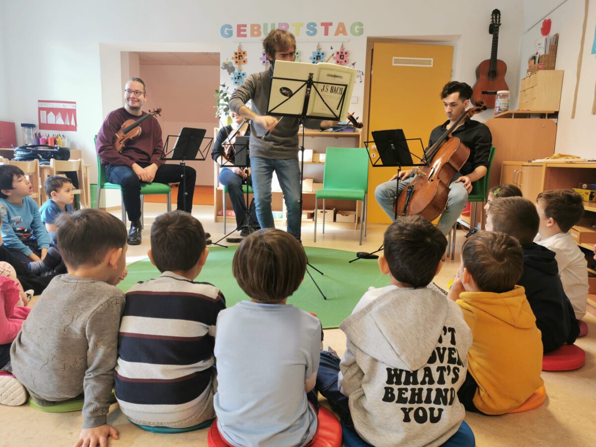 Ein Streichquartett spielt in einem Klassenraum. Um sie sitzen einige Kinder in einem Halbkreis.
