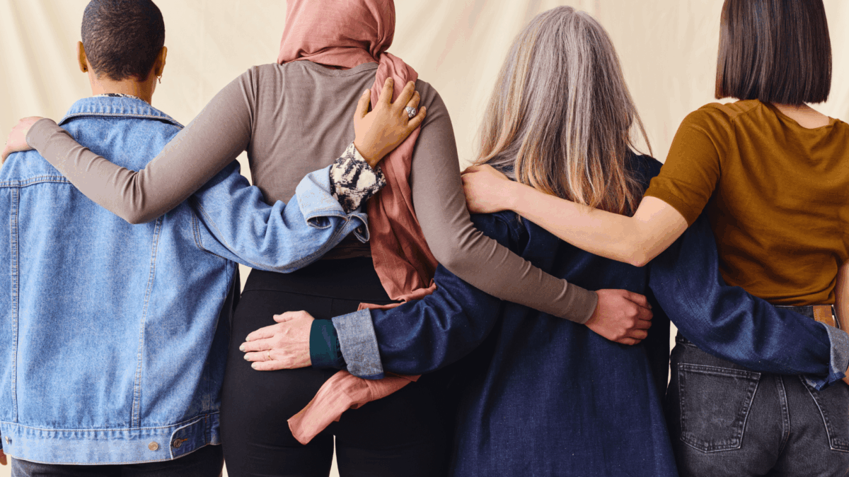 Symbolbild: Frauen (von hinter gesehen) stehen in einer Reihe und umarmen sich.