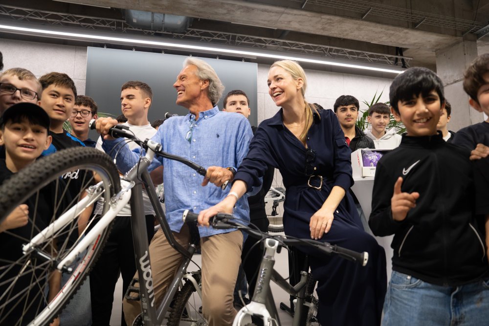 Oliver Stamm und Silvia Bruni posieren mit zwei Fahrrädern und einigen Kids für ein Gruppenfoto.