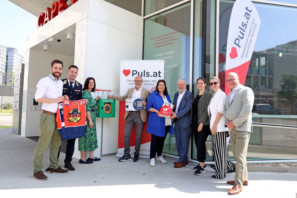 Elfriede Wittberger, Siegfried Meryn, Silvia Bruni und einige Vertreter:innen des Verein PULS posieren mit dem Defibrillator vor dem Haupteingang von CAPE 10.