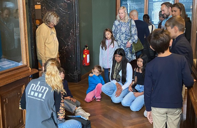 Einige Familien und ihre Kinder lauschen einer Mitarbeiterin des Naturhistorischen Museums Wien.