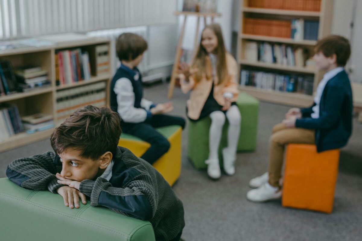 Symbolbild: Im Fokus eine junge der trauriger aussieht. Im verschwommenen Hintergrund eine Gruppe Kinder die lacht.
