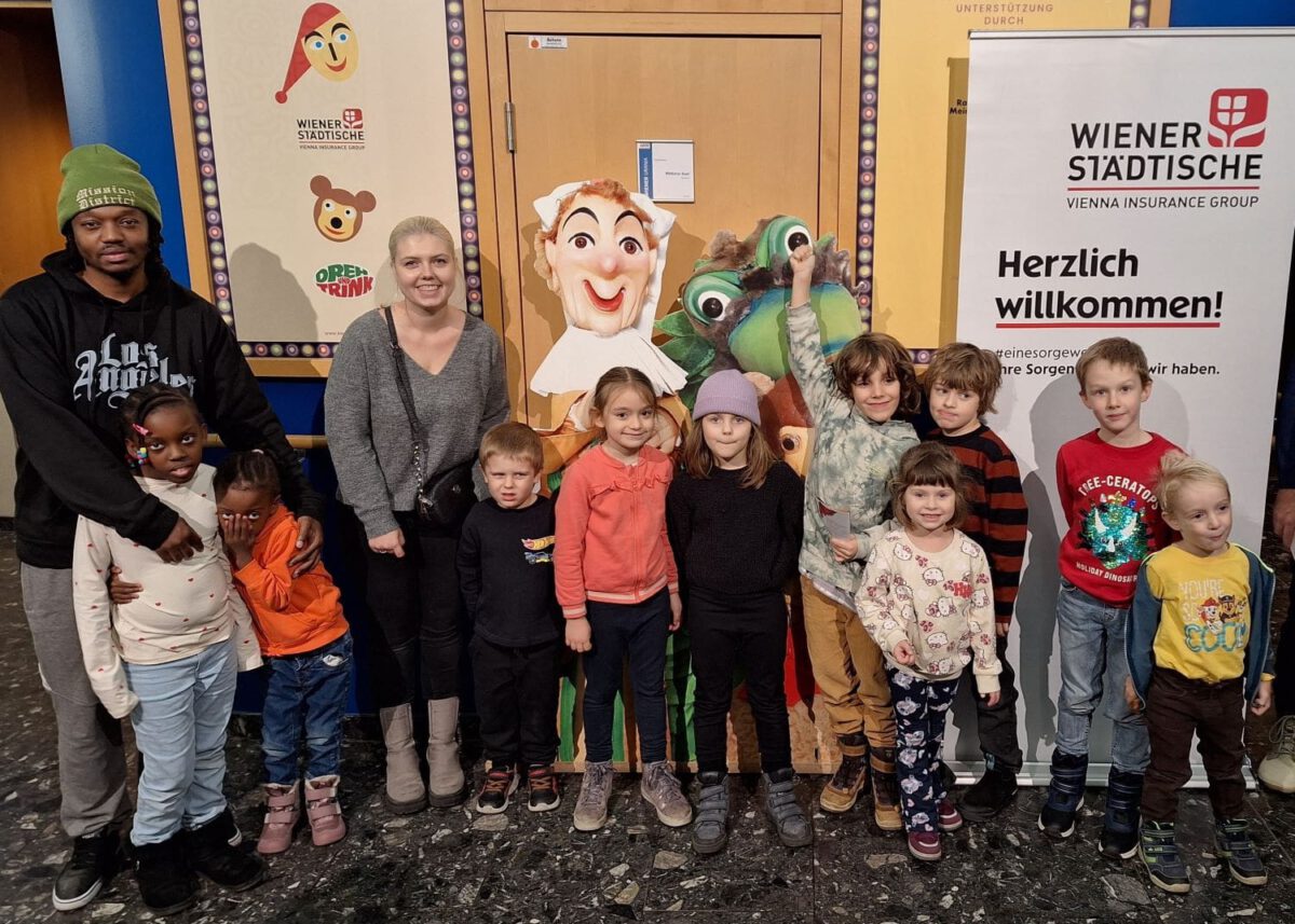 Kinder und Erwachsene vor dem Eingang zur Kasperl-und-Pezi-Vorstellung, Plakate der Wiener Städtische sind im Hintergrund.