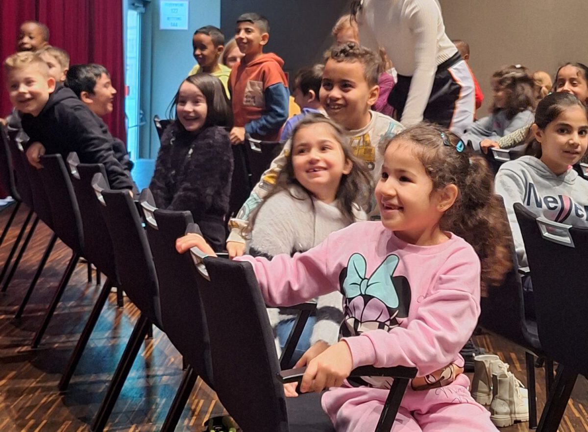 Einige Kinder sitzen in der Zuschauerreihen des Volkstheater Wien und beobachten lachend das Stück.