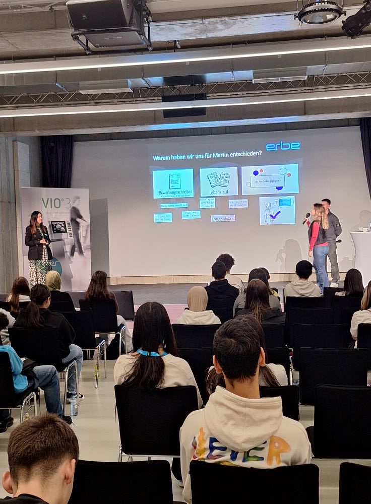 Auf der Bühne im CAPE 10 wird ein Vortrag von Erbe Elektromedizin abgehalten. Im Publikum sitzen die Schüler:innen der MIM Wendstattgasse.