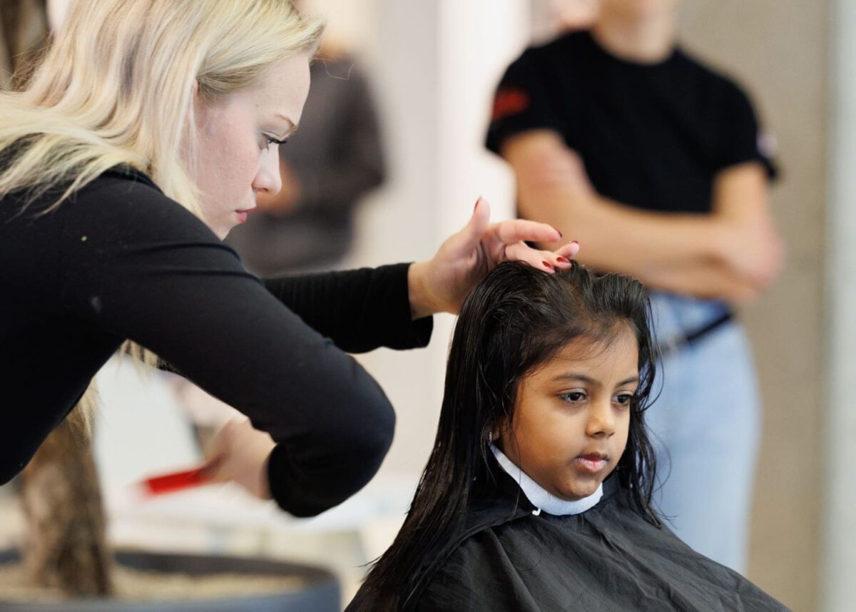 Eine Frisörin schneidet einem jungen Mädchen die Haare.