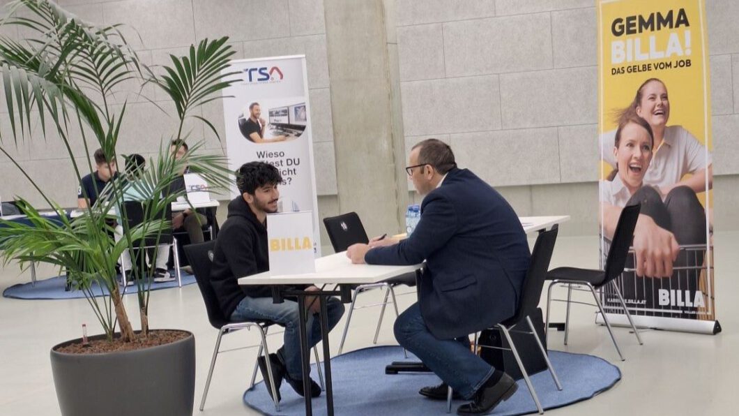 Ein Mitarbeiter von BILLA und ein Jugendlicher sitzen gegenüber an einem Tisch und führen ein Bewerbungsgespräch.