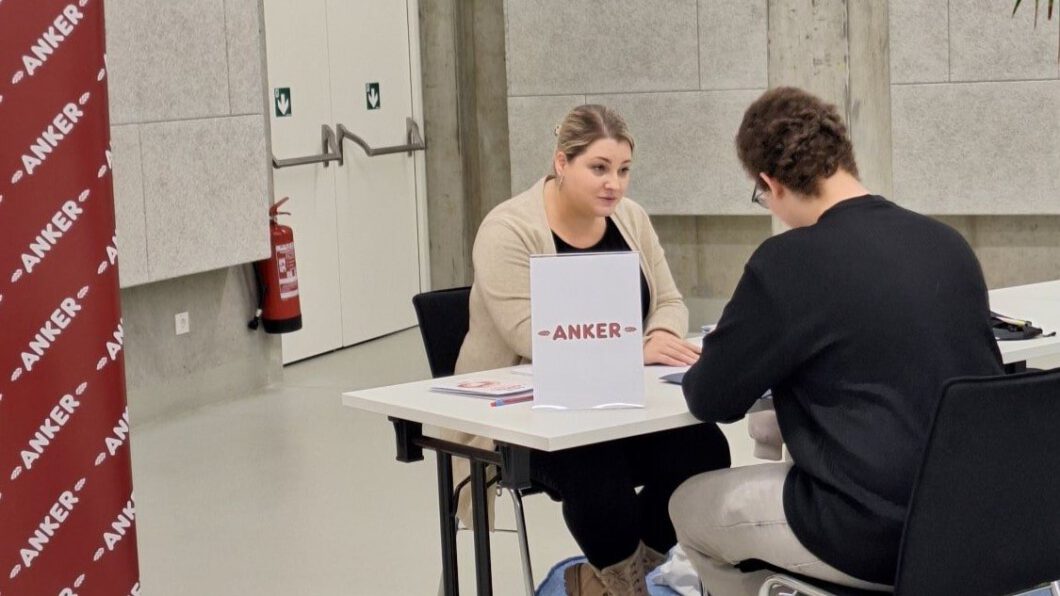 Eine Mitarbeiterin von ANKER und ein Jugendlicher sitzen gegenüber an einem Tisch und führen ein Bewerbungsgespräch.
