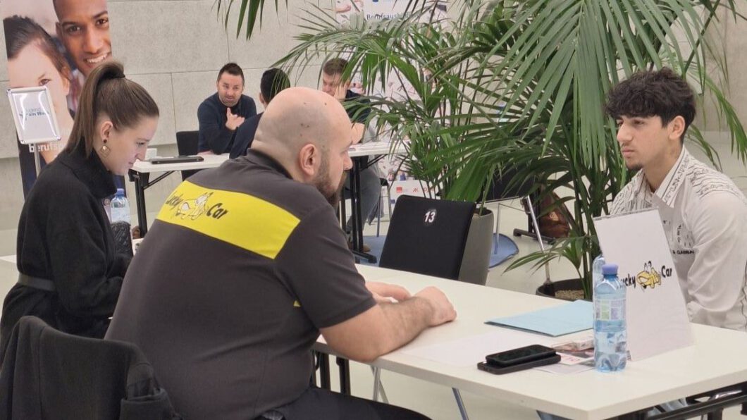 Eine Mitarbeiterin und ein Mitarbeiter von Lucky Car und ein Jugendlicher sitzen gegenüber an einem Tisch und führen ein Bewerbungsgespräch.