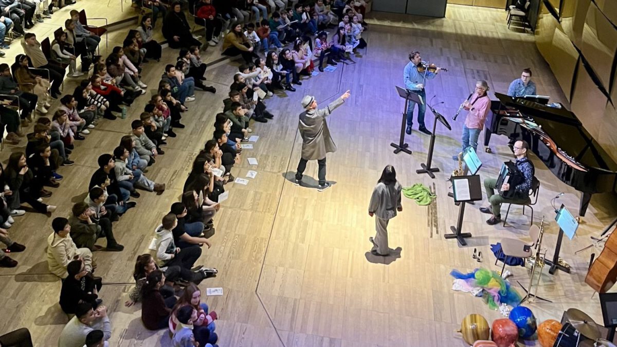 Kinder sitzen im Halbkreis um ein Orchester und lauschen der Musik.