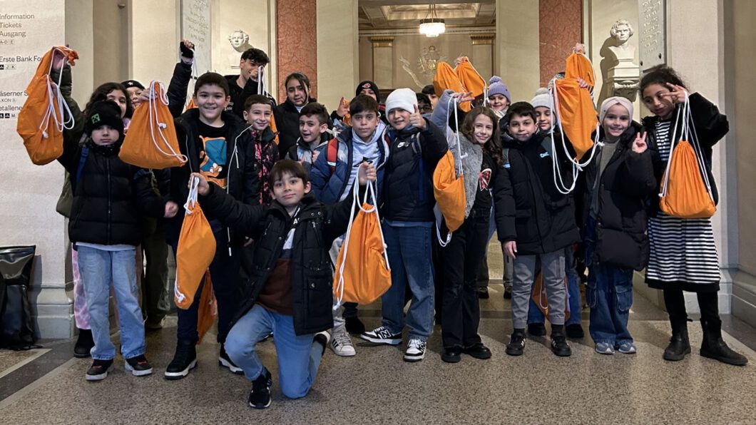 Eine Gruppe von Kindern posiert für ein Gruppenfoto mit orangenen Wien Energie Turnbeuteln.