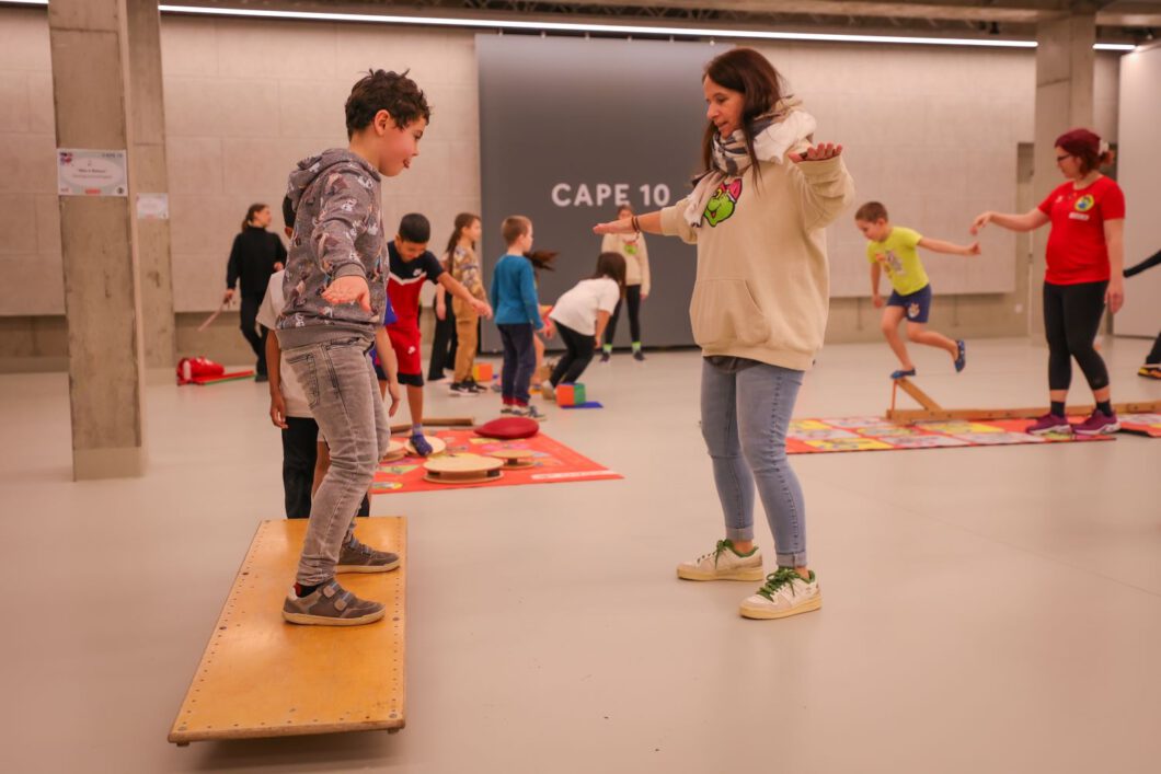 Ein Bub steht mit auf einem Balance-Board, gegenüber
von ihm steht eine Betreuerin und zeigt ihm wie die Balance hält.