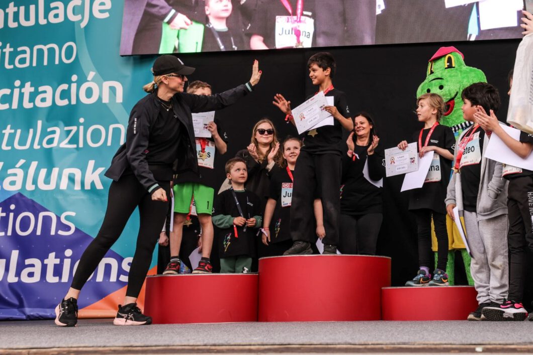 Junge mit Urkunde bekommt beim Vienna City Marathon ein High Five von Silvia Bruni, andere Kinder mit Medaillen applaudieren.
