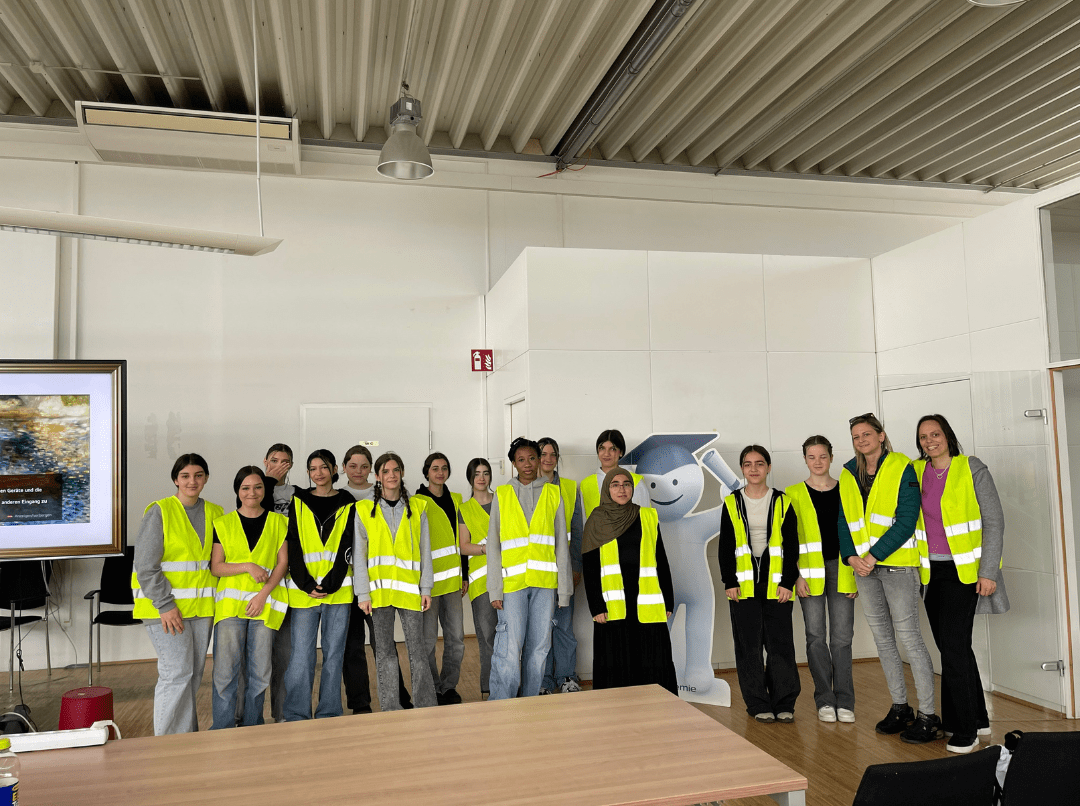 Eine Gruppe von Schülerinnen in gelben Sicherheitswesten steht in einem Innenraum und posiert für ein Gruppenfoto.