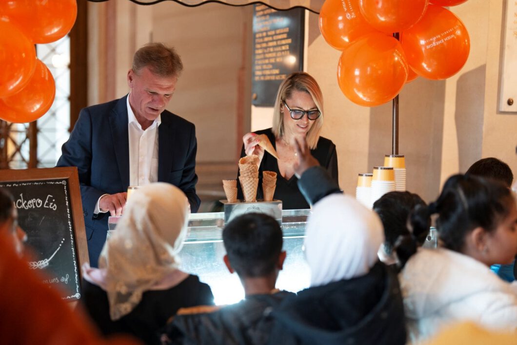 Silvia Bruni und Michael Strebl stehen hinter einem Eiswagen und geben Eis an Volksschulkinder aus.