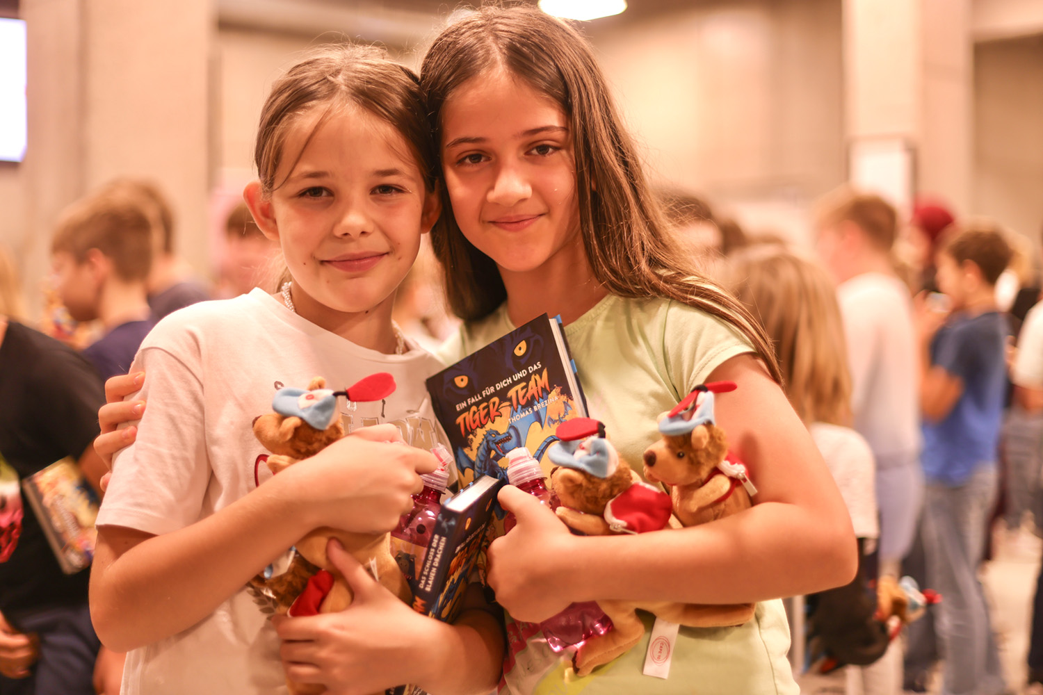 Zwei Mädchen posieren lachend mit Känguru-Stofftieren und Thomas Brezina Büchern.