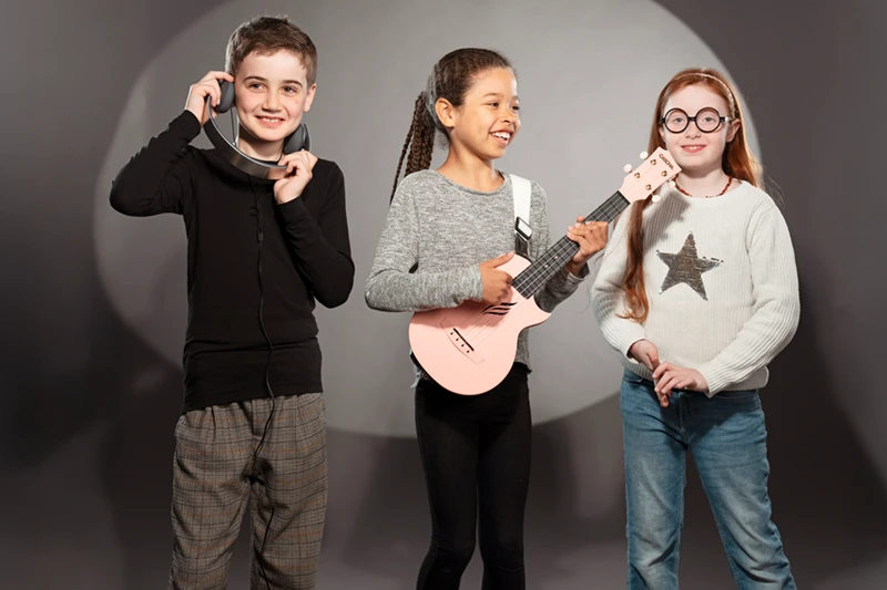 Drei Kinder mit Kopfhörer, Gitarre und Drumsticks. Symbolbild für CAPE 10-Chancenpaket.