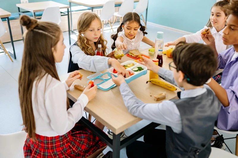 Schulkinder essen gemeinsam am Tisch. Symbolbild für CAPE 10-Initiative "Herz und Bauch".