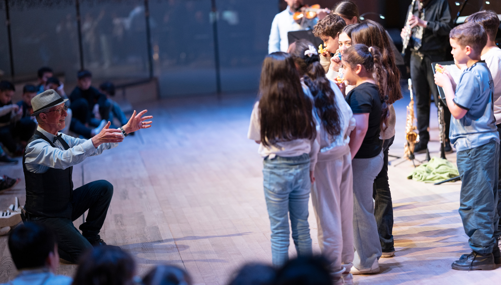Kinder stehen auf der Bühne im Musikverein und lauschen gespannt Albert Landertinger.