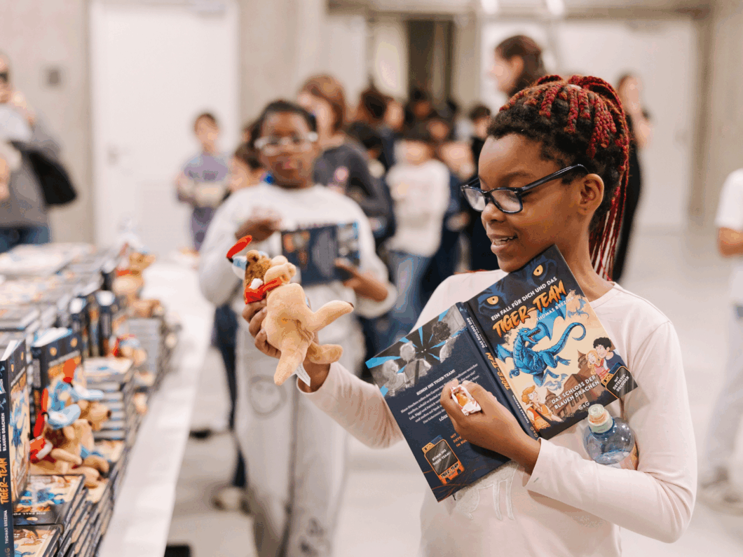 Ein Mädchen der Kinderbuchlesung mit einem geschenkten Buch und dem Cäpi Stofftier.
