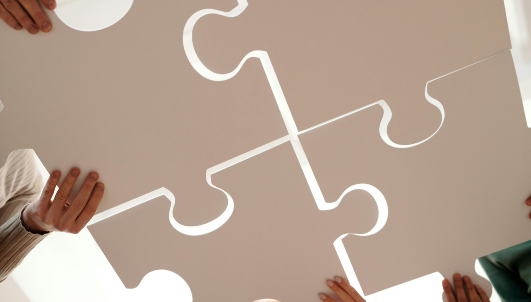 Personen fügen übergroße Puzzlestücke zu einem großen Ganzen zusammen.