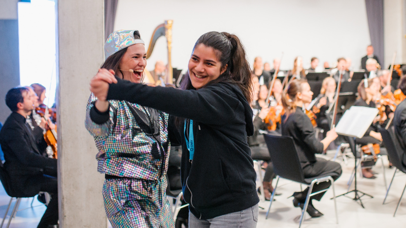 Eine Frau und ein Mädchen tanzen miteinander und lachen dabei,