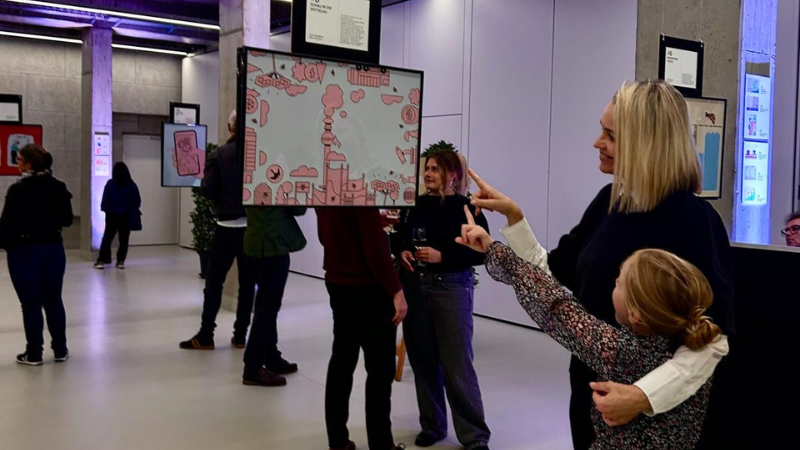 Eine Frau und ein Mädchen bestaunen ein Gemälde. Beide zeigen mit dem Zeigefinger auf das Bild und lächeln.