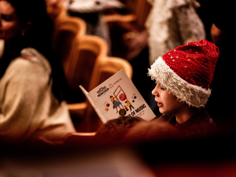 Ein Junge mit einer roten Weihnachtsmütze liest in einem Programmheft mit der Aufschrift "The Power of Music".