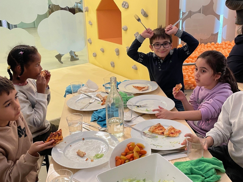 Kinder sitzen an einem Tisch in der CAPE 10 Kinderwelt beim gemeinsamen Mittagessen.
