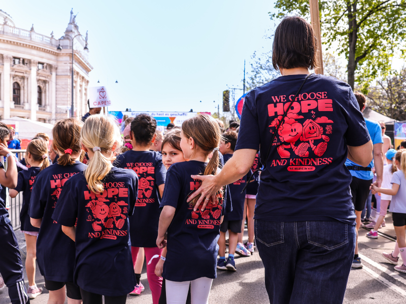 Kinder gehen mit eine Betreuerin zum Start des VCM-Laufs. Die Aufnahme ist von hinten.