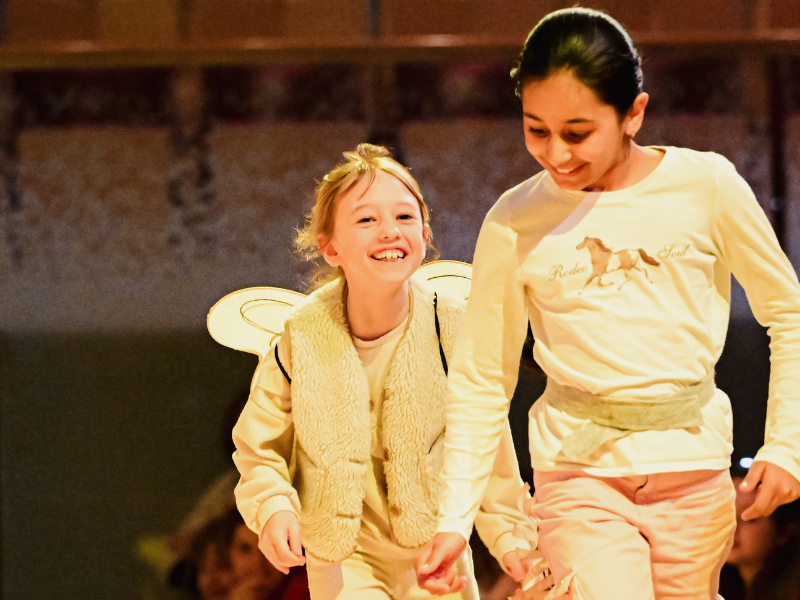 Zwei Mädchen lachen und gehen hintereinander. Ein Mädchen hat Schmetterlingsflügel auf dem Rücken.