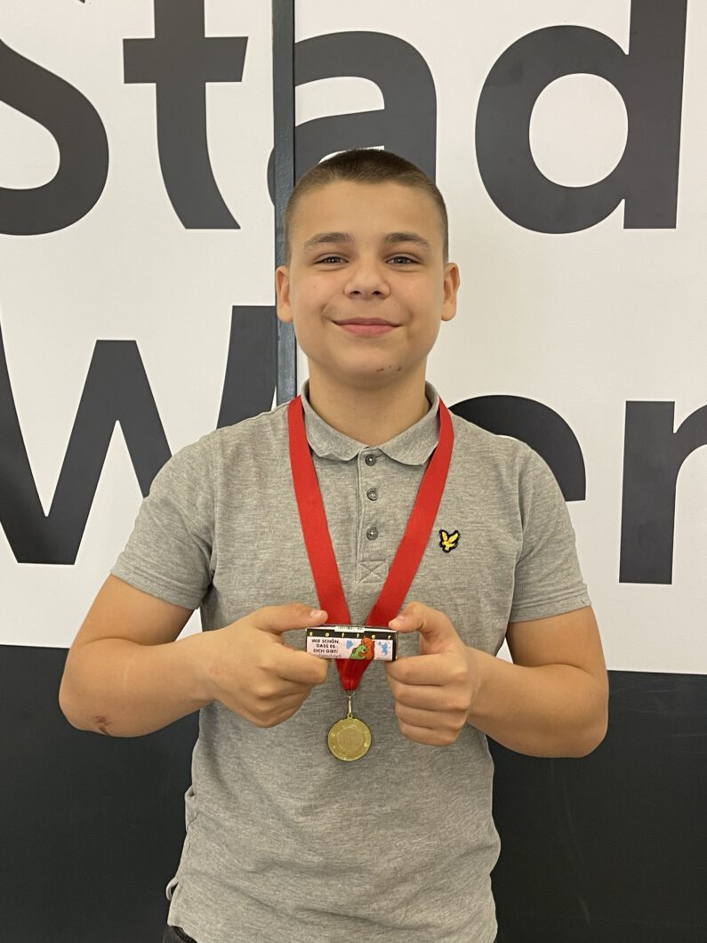 Ein Junge posiert mit einer CAPE 10 Medaille um den Hals. In den Händen hält er eine Schokolade mit der Aufschrift: "Wie schön, dass es dich gibt".